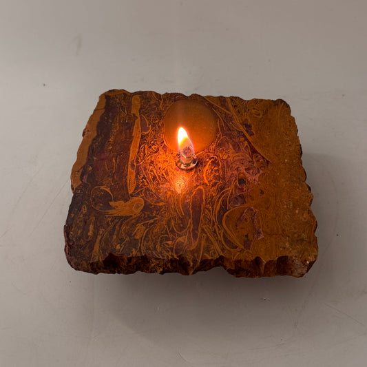 Orange oil candle stone rock with lit wick in center, decorative calligraphy