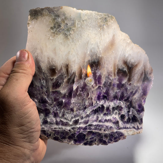 Hand holding amethyst geode slab candle with flame on purple crystal stone