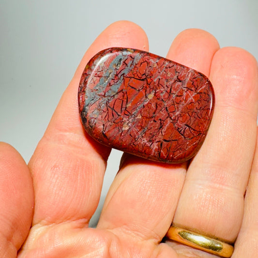 Red-orange jasper knob with cracked stone pattern held in hand; visible black base
