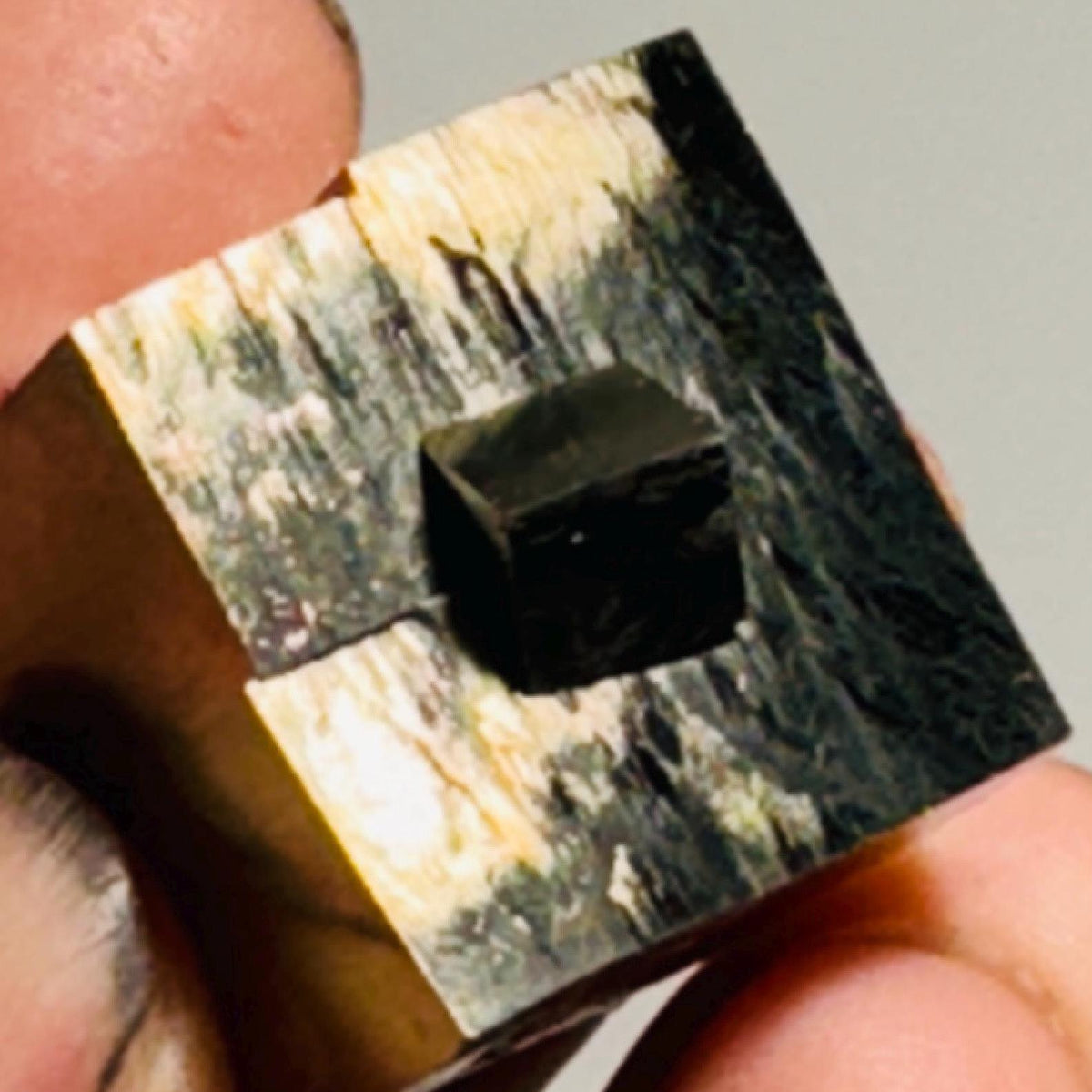 Close-up pyrite cube showing dark square cavity, reflective metallic gold surface.