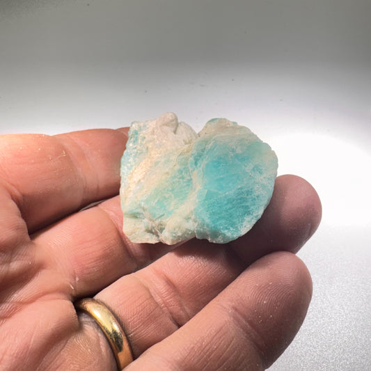 Amazonite crystal rough stone held in hand, teal-blue and white matrix