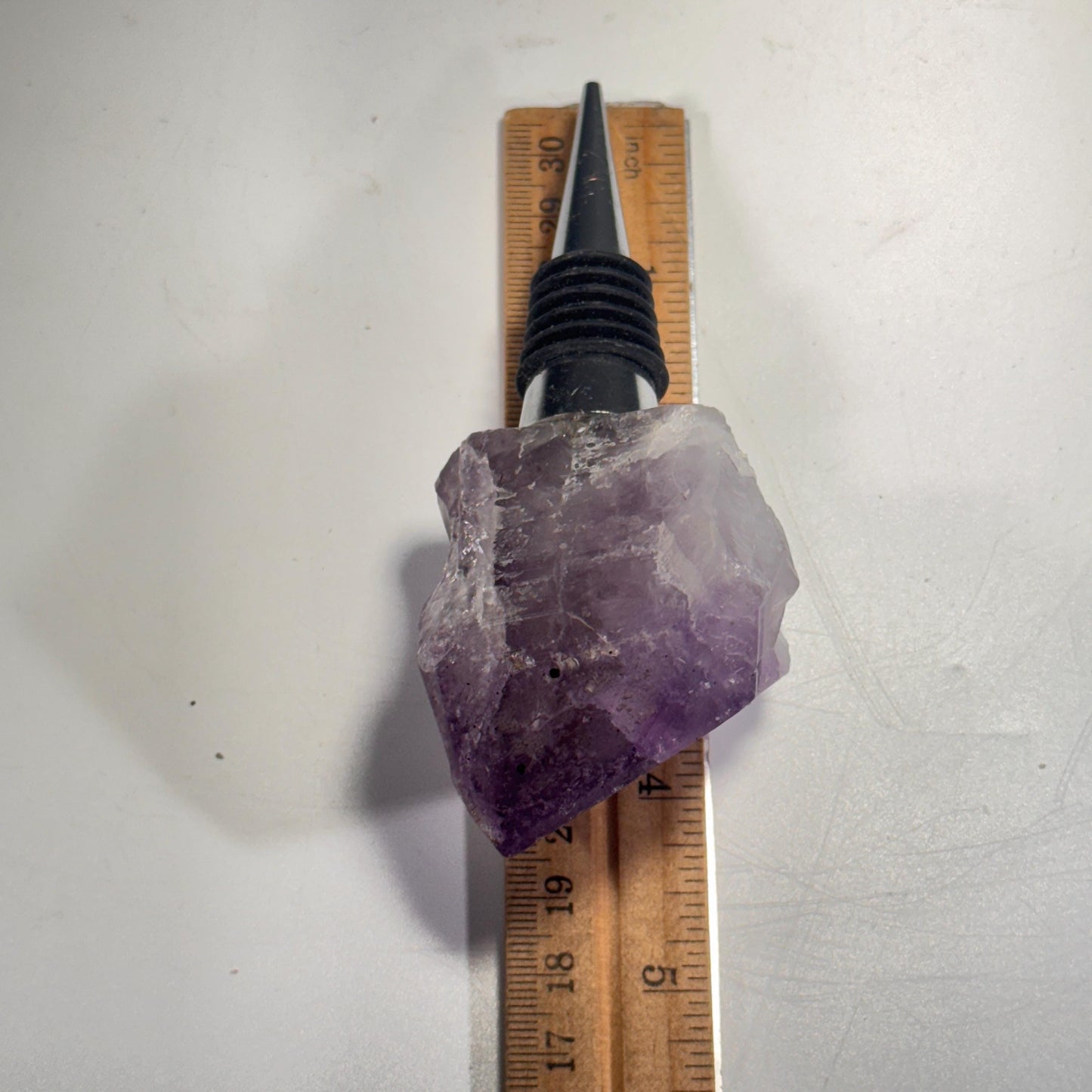 Purple crystal bottle stopper measured on ruler, black ribbed plug and metal tips