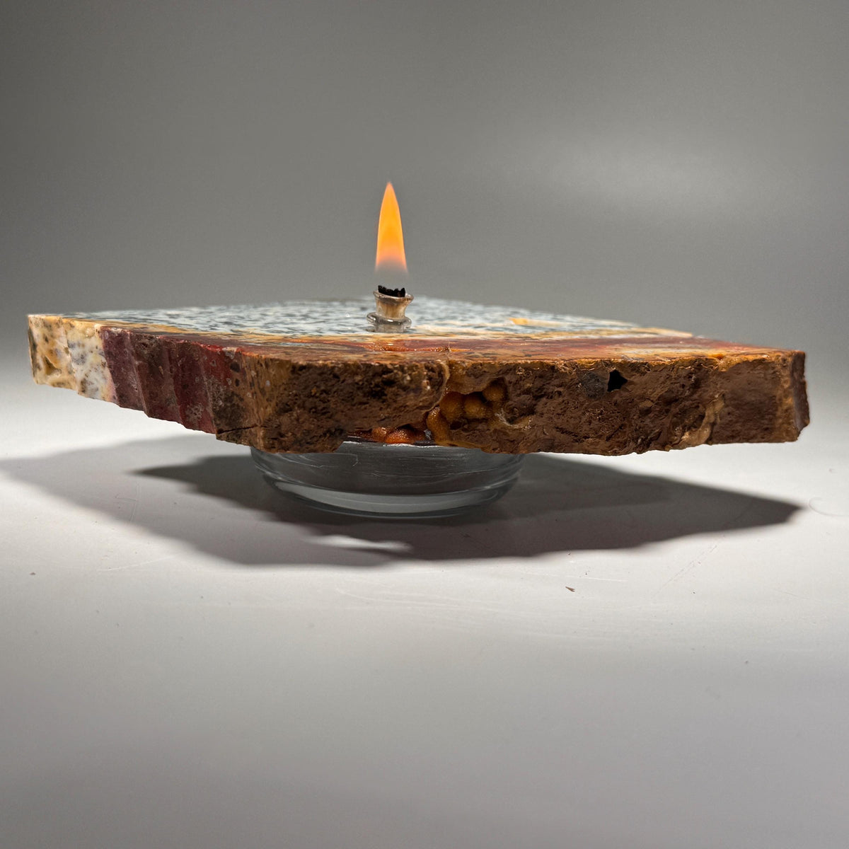 Agate rock candle with upright flame on rustic slab; glass holder underneath