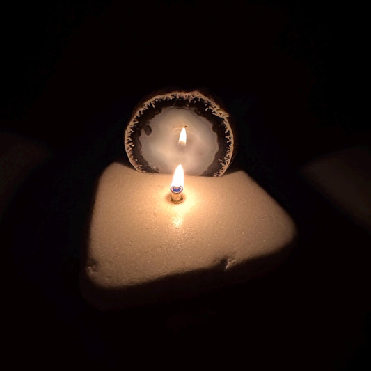 Agate geode rock candle with lit wick centered on white stone base