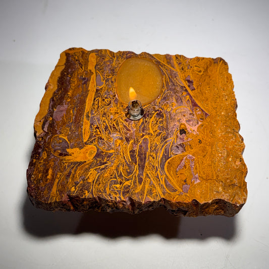 Orange oil candle stone rock with lit wick and embossed round wax center