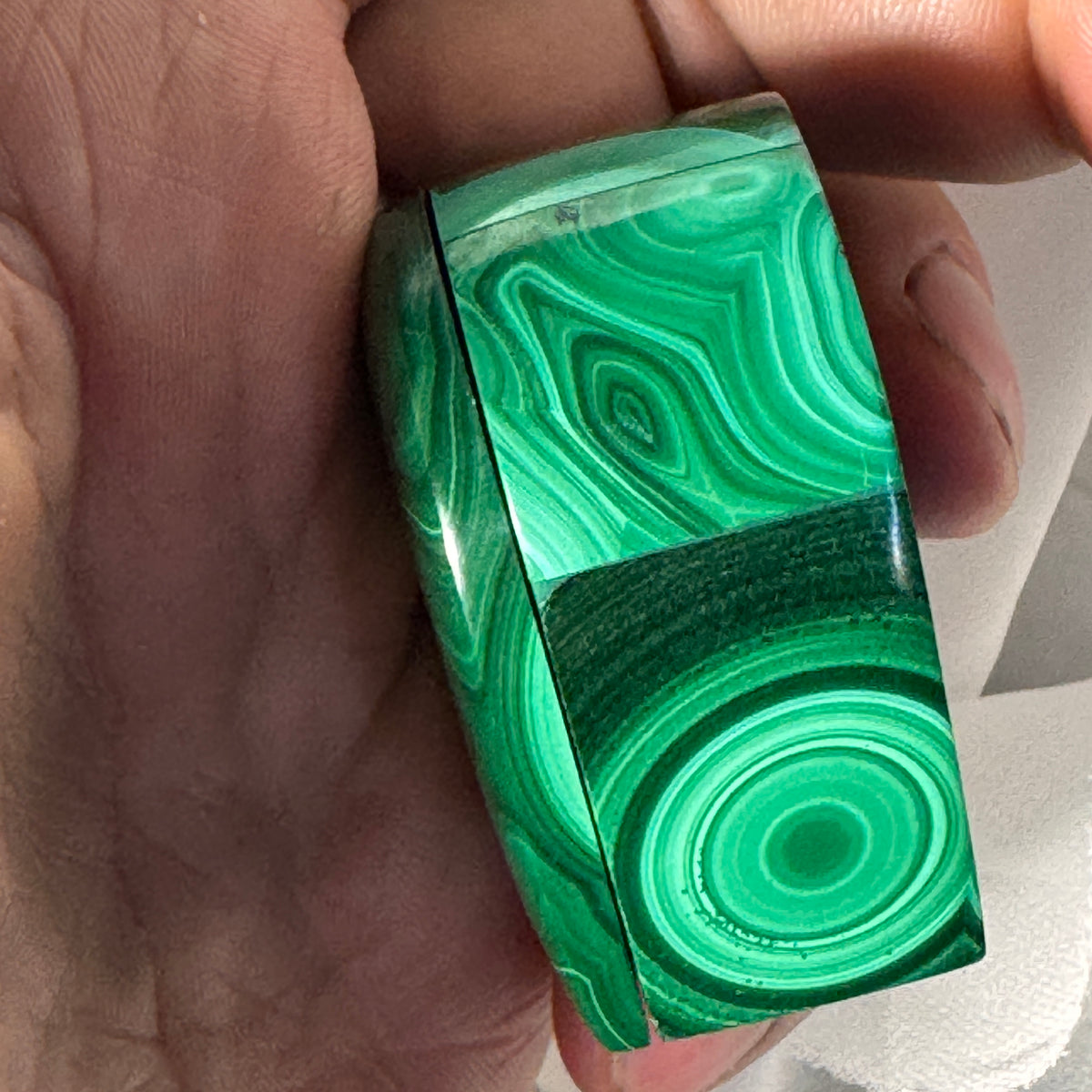 Small malachite heart box held in hand, glossy green patterns and dark hinge line