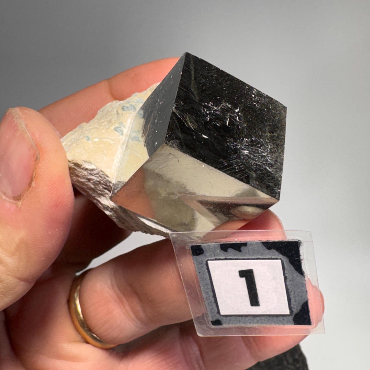 Handheld pyrite cube with black metallic face set in tan rock matrix