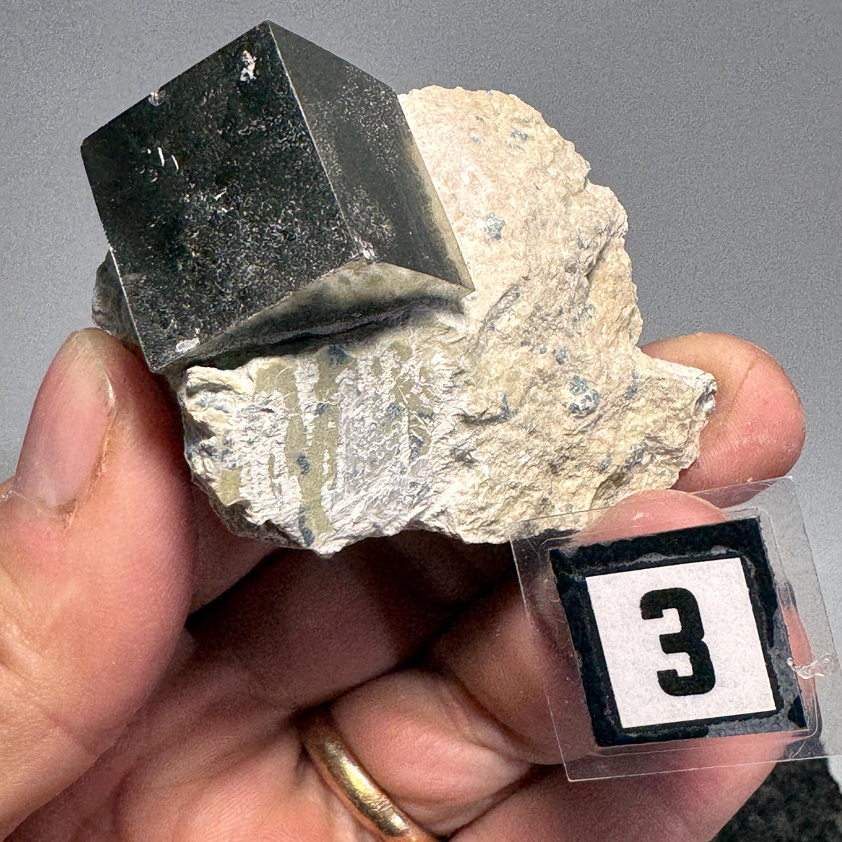 Handheld pyrite cube with black crystal face in light tan matrix