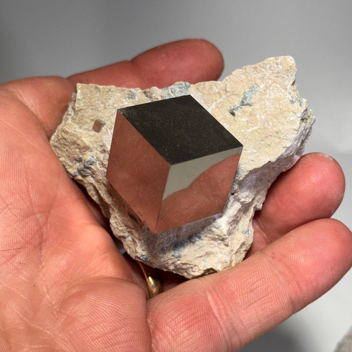 Pyrite crystal in matrix held in hand, showing dark cube facets