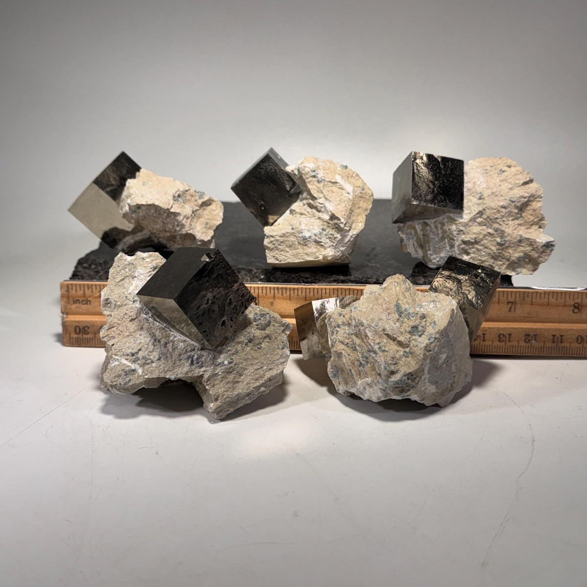 Multiple pyrite cube clusters arranged on flat surface with scale marks